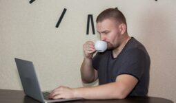 a man drinking a cup of coffee while using a laptop
